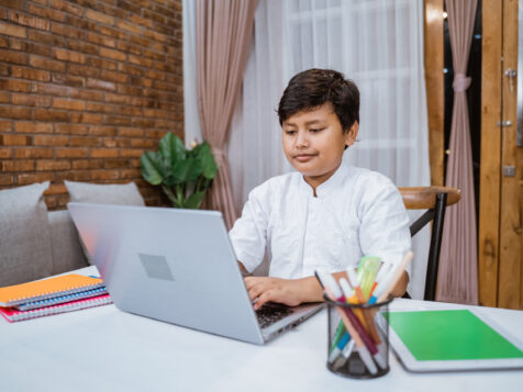 Cheerful boy writing using laptop while doing schoolwork memorize-quran-online-in-hong-kong