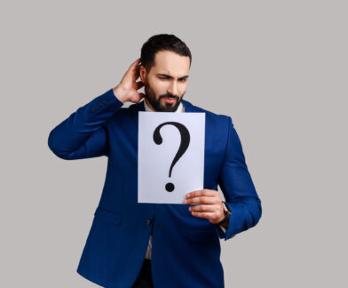 Confused bearded man holds question mark, finding smart solution